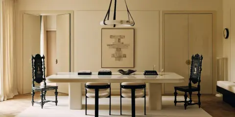 Comedor elegante con mesa blanca, sillas negras y una paleta de colores crema. Arte abstracto y cortinas suaves complementan el espacio.