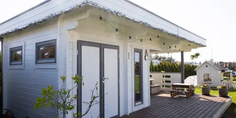 Una cabaña de madera con terraza, ideal para hacer una habitación en una terraza. Luces decorativas cuelgan del techo.