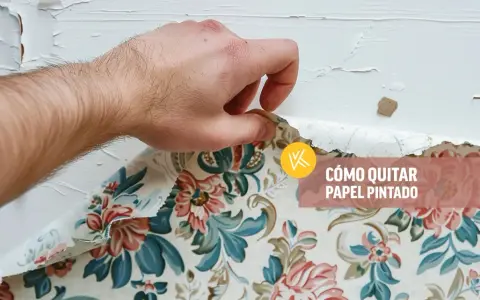 Mano retirando papel pintado floral de una pared blanca. Aprende cómo quitar papel pintado sin dañar la pared.