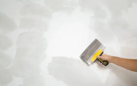 Mano con espátula trabajando en pared rugosa, como quitar pintura.