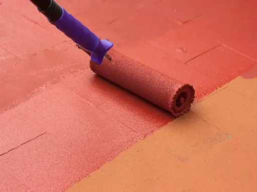 Rodillo pintando suelo de patio exterior con pintura roja, renovando el espacio.
