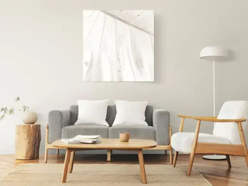 Un cuadro de hoja en tonos claros decora la pared, complementando el estilo zen de los cuadros feng shui dormitorio. Sofá gris, sillón blanco y mesa de centro de madera.