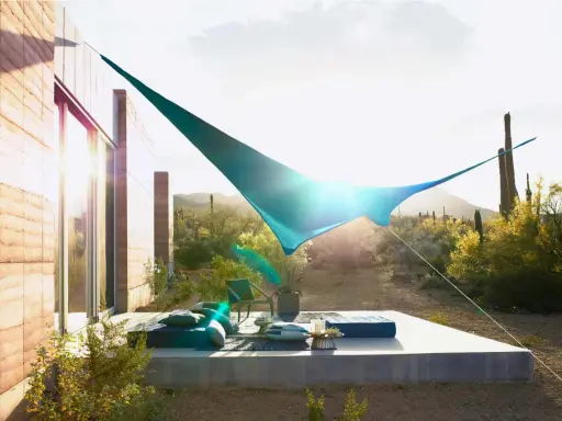 Ideas de sombra para terraza desértica: una vela azul crea un oasis fresco sobre cojines y un sillón.