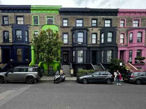 Fila de casas de colores vibrantes en Londres, con fachadas azules, verdes y rosas, estacionadas junto a coches y una moto.