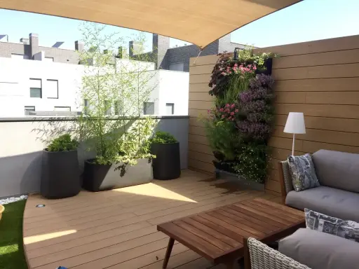 Un **jardín moderno** en una terraza con sofá, mesa de madera, plantas en macetas y un muro verde vibrante.