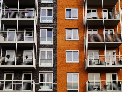 Fachada de edificio moderno con ladrillo naranja y oscuro, balcones blancos y ventanas. Un proyecto de reforma fachada casa que realza su estética.