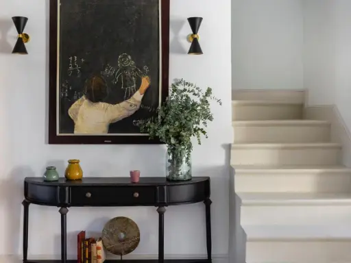 Entrada de una casa pequeña con consola negra, cuadro de tiza y escaleras. Un toque de feng shui casa pequeña para armonizar el espacio.