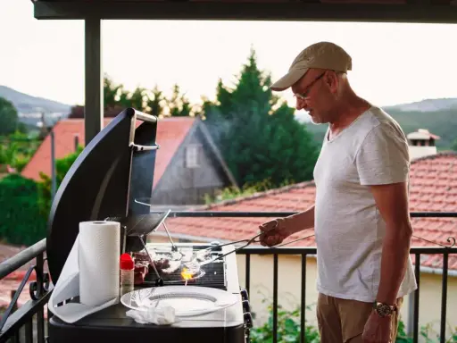 Hombre preparando barbacoa en patio interior con vistas a un pueblo.