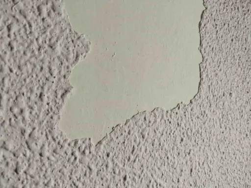 Detalle de pared con gotelé descascarillado, mostrando la capa inferior lisa. Ideal para aprender como quitar gotele.