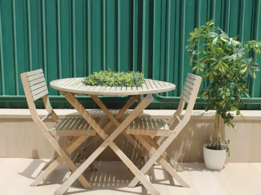 Conjunto de madera para dos personas en unas terrazas pequeñas con encanto. Una planta verde decora el rincón.