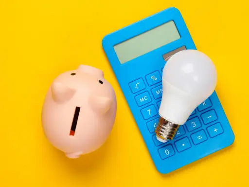 Hucha rosa, calculadora azul y bombilla LED. Ideas para como ahorrar en la factura del gas y la luz.
