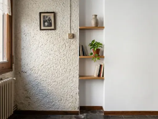 Un rincón con paredes lisas y otra con gotele, un retrato familiar, estanterías con libros y una planta.