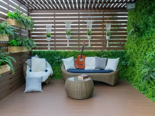 Terraza acogedora con muebles de mimbre, plantas colgantes y una pared verde. Ideal para relajarse, como cubrir una terraza con poco dinero.