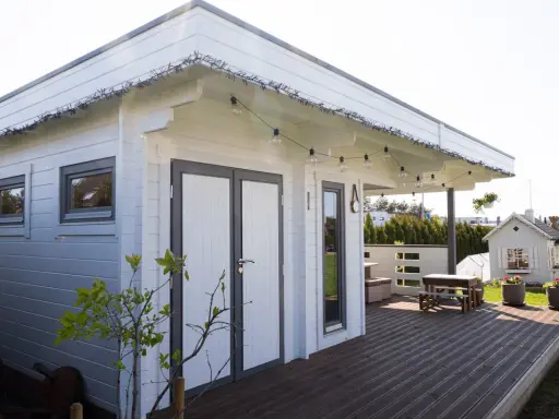 Una cabaña de madera con terraza, ideal para hacer una habitación en una terraza. Luces decorativas cuelgan del techo.