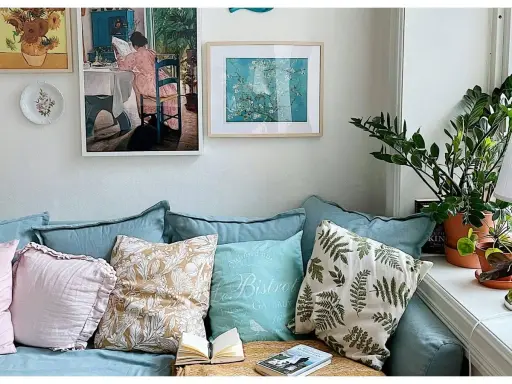 Acogedor rincón de plantas en el salón, con un sofá azul, cojines decorativos y cuadros en la pared.