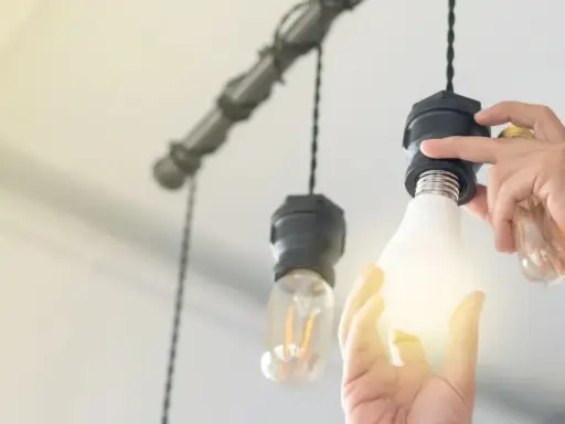 Manos cambian una bombilla LED por una incandescente en una lámpara colgante, actualizando la luz del hogar.