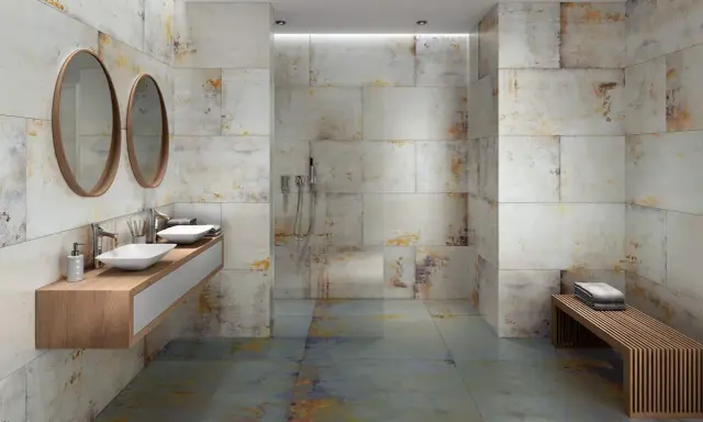 Baño moderno con paredes y suelo de baldosas grises y oxidadas. Los tonos tierra y dorados de las baldosas muestran que colores combinan con el gris en un baño.