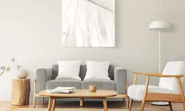 Un cuadro de hoja en tonos claros decora la pared, complementando el estilo zen de los cuadros feng shui dormitorio. Sofá gris, sillón blanco y mesa de centro de madera.