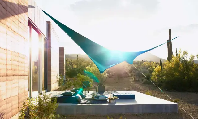 Ideas de sombra para terraza desértica: una vela azul crea un oasis fresco sobre cojines y un sillón.