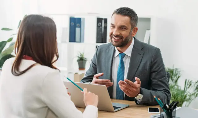 Un hombre sonriente, que parece ser un asesor energético, explica algo a una mujer en una oficina.