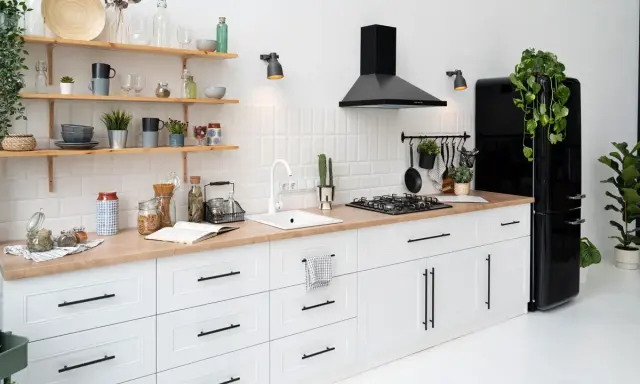 Cocina moderna con gabinetes blancos y encimera de madera. El diseño para pintar cocinas es minimalista, con electrodomésticos negros y estantes de madera.