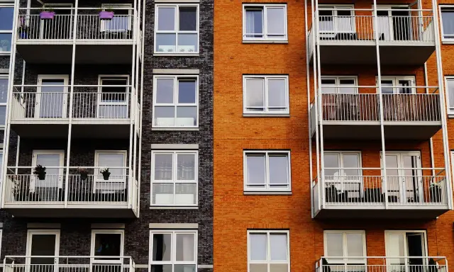 Fachada de edificio moderno con ladrillo naranja y oscuro, balcones blancos y ventanas. Un proyecto de reforma fachada casa que realza su estética.