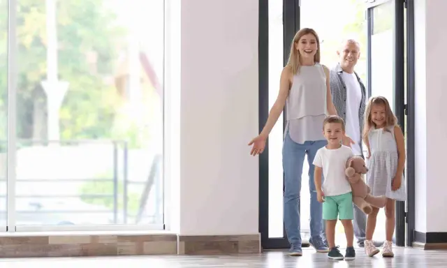 Familia de 4 miembros sonriendo y entrando a su nuevo hogar, pensando en el consumo medio electricidad.