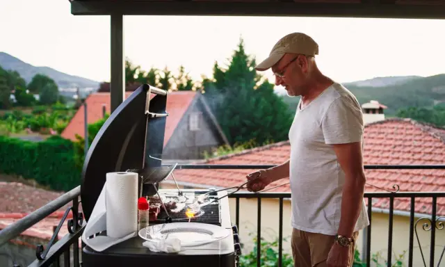 Hombre preparando barbacoa en patio interior con vistas a un pueblo.
