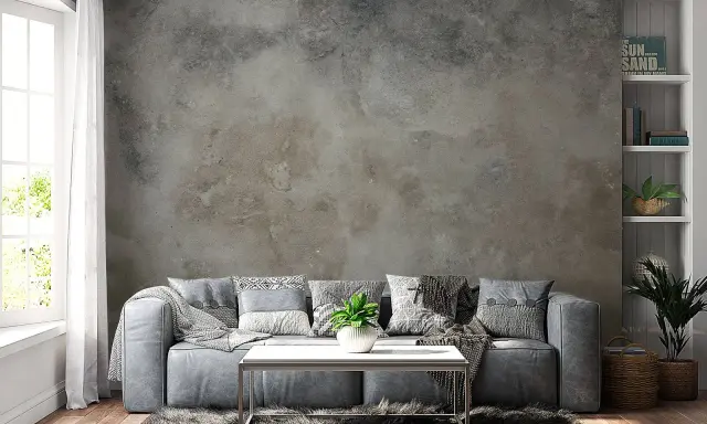Sofá gris frente a una pared con efecto de pintar pared efecto envejecido. Alfombra peluda y mesa de centro metálica.