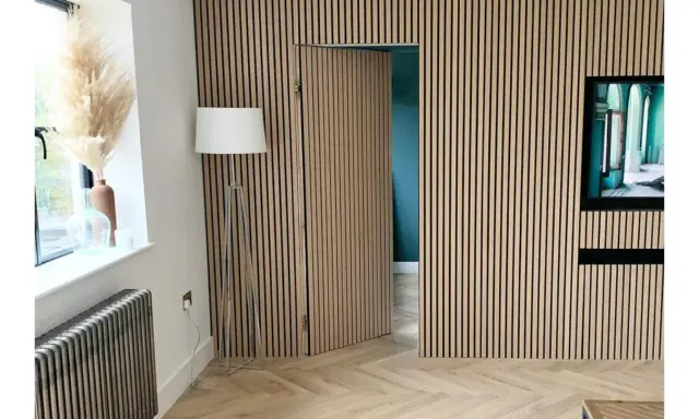 Una puerta oculta en una pared revestida de lamas de madera, una solución ingeniosa para como ocultar una puerta en una pared.