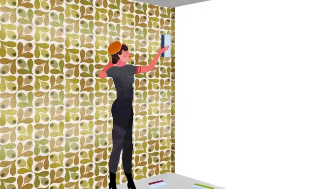 Mujer con boina naranja aplica papel tapiz con diseño de olivas. Muestra por dónde empezar a empapelar una pared, con herramientas en el suelo.