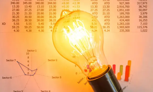 Bombilla incandescente sobre gráficos y tablas. ¿Qué es la tarifa indexada luz? Representa la fluctuación de precios en el mercado eléctrico.