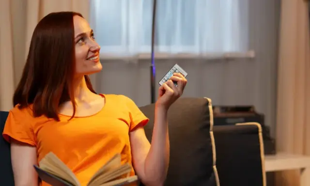 Mujer sonríe con un control remoto en mano, pensando que 800 kWh es mucho para su factura de luz.