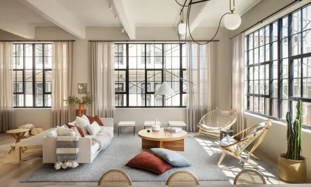 Salón con estilo industrial nórdico: sofá blanco, mesas de centro de madera, sillas de ratán y grandes ventanales.