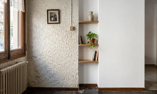 Un rincón con paredes lisas y otra con gotele, un retrato familiar, estanterías con libros y una planta.