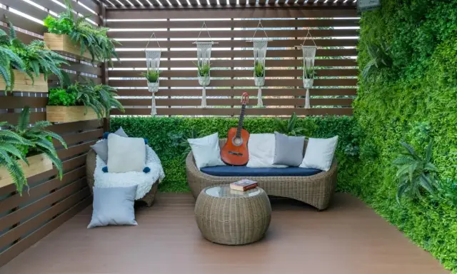 Terraza acogedora con muebles de mimbre, plantas colgantes y una pared verde. Ideal para relajarse, como cubrir una terraza con poco dinero.