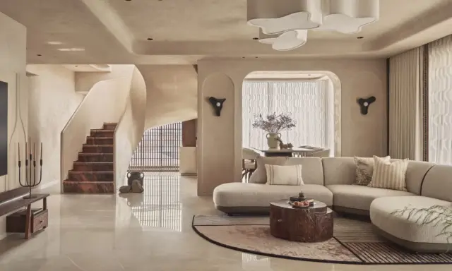 Salón con sofá curvo, mesa de centro de tronco y escaleras de mármol. Un espacio con estilo vanguardista y acabados orgánicos.