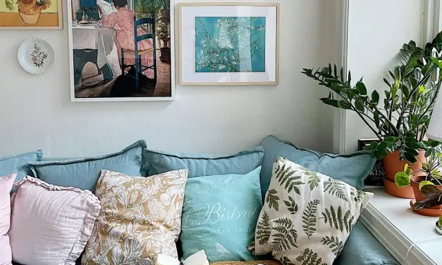 Acogedor rincón de plantas en el salón, con un sofá azul, cojines decorativos y cuadros en la pared.