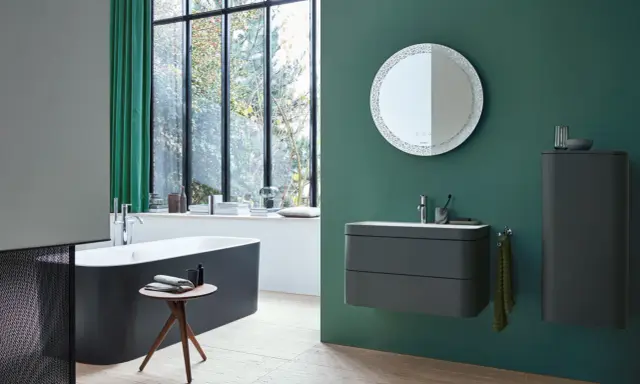 Un baño moderno con bañera oscura, lavabo flotante y espejo decorativo. La pared verde es un lienzo perfecto para pintar el baño.