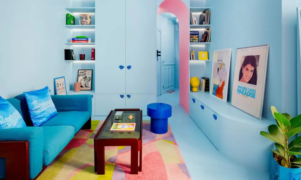 Salón pequeño con sofá azul, alfombra geométrica y estanterías llenas de objetos. Los colores pastel y vibrantes son ideales como colores para pintar salones pequeños.