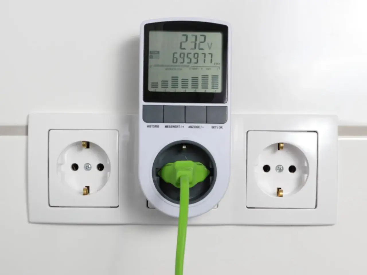 Medidor de consumo el&eacute;ctrico enchufado a una toma de corriente. Muestra voltaje y kWh, ayudando a entender como se mide el consumo electrico.