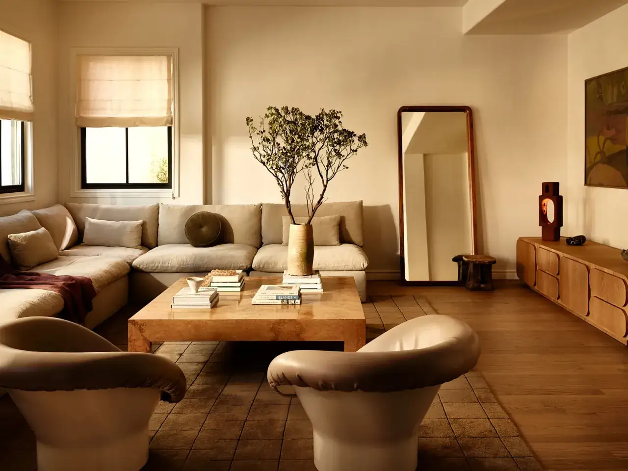 Sof&aacute; modular y sillones en una sala de estar con una paleta de colores crema, mesa de centro de madera y espejo de cuerpo entero.