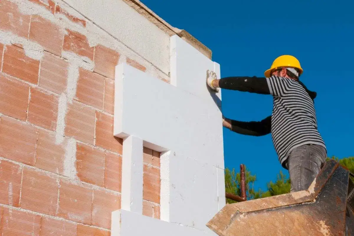 Obrero coloca poliestireno para reformar fachada casa. Aislamiento térmico en construcción.