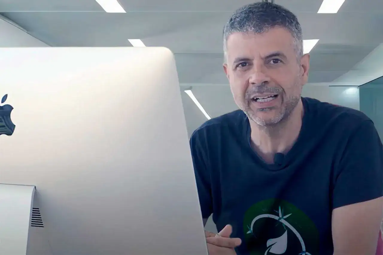 Hombre con barba gris habla frente a un iMac. Podría ser un asesor energético explicando cómo optimizar el consumo.