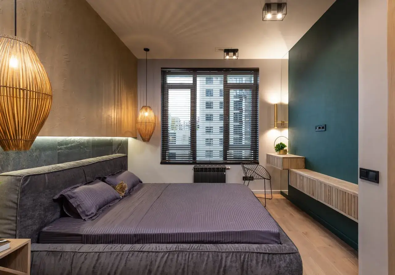 Elegante habitación con cama gris, lámparas de mimbre y pared verde. Los colores de la habitación crean un ambiente acogedor y moderno.