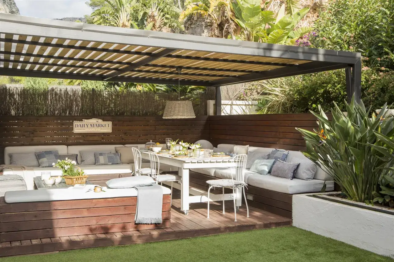 Espacio exterior con varios tipos de pergolas, asientos cómodos y mesa lista para comer.