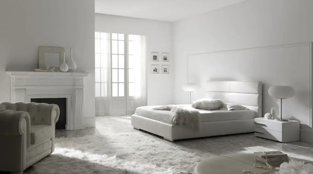 Dormitorio minimalista con cama blanca, chimenea y sillón. Los colores que dan luz y amplitud crean un ambiente sereno y acogedor.