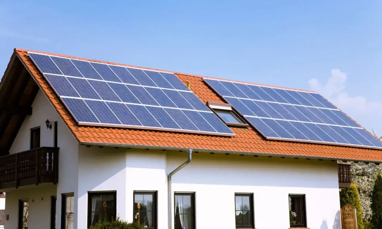 Casa con tejado de tejas naranjas y varias placas fotovoltaicas azules captando la luz del sol.
