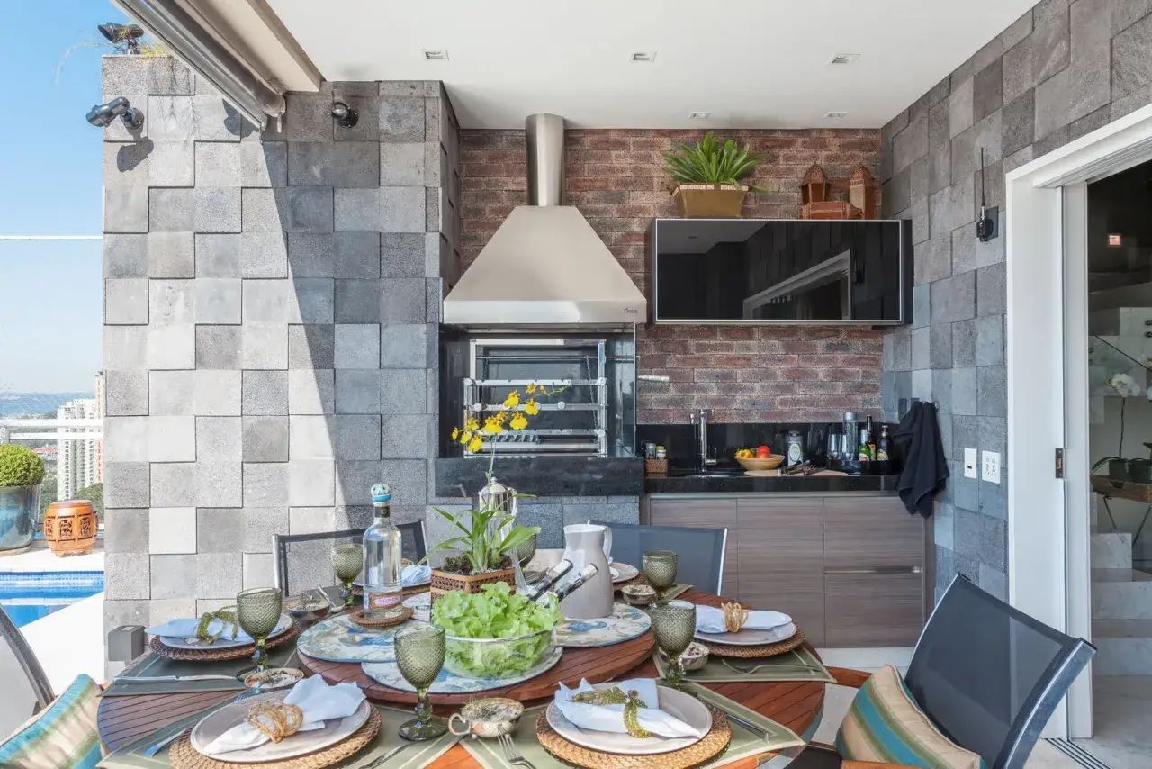 Mesa puesta para una barbacoa en un patio interior, con parrilla, TV y vistas a la ciudad.