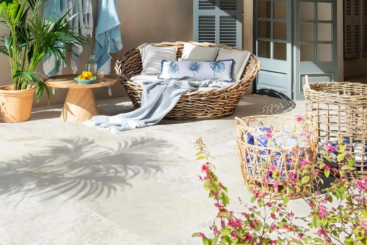 Cómoda terraza cubierta piso con sillón de mimbre, mesa auxiliar de madera, plantas y cestas.